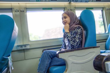 Tren vagonunda yolcu koltuğunda oturan mutlu Asyalı Müslüman kadın. traleving kavramı