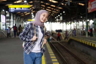 Tren istasyonunda durup treni bekleyen mutlu Asyalı Müslüman kadın. seyahat kavramı