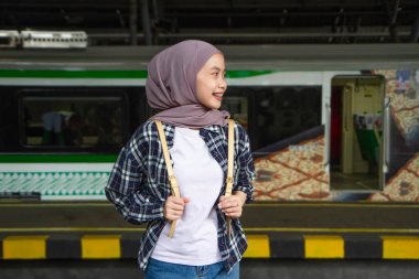 Tren istasyonunda durup treni bekleyen mutlu Asyalı Müslüman kadın. seyahat kavramı