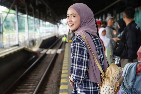 Tren istasyonunda durup treni bekleyen mutlu Asyalı Müslüman kadın. seyahat kavramı  