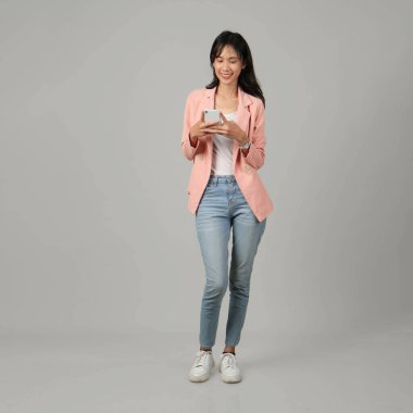 Cep telefonu tutan mutlu Asyalı kadının uzun bir çekimi. Ayrı bir arkaplanda resmi kıyafet giymek