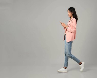 Tam uzunlukta, resmi kıyafet giymiş Asyalı kadınları çek, cep telefonuyla yürüyen bir jest yap, izole edilmiş arka planda.