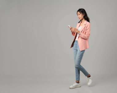 Tam uzunlukta, resmi kıyafet giymiş Asyalı kadınları çek, cep telefonuyla yürüyen bir jest yap, izole edilmiş arka planda.