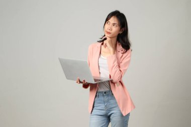 Düşünceli Asyalı bir kadın dizüstü bilgisayarı elinde tutuyor ve izole edilmiş arka planda bir jest yapıyor.