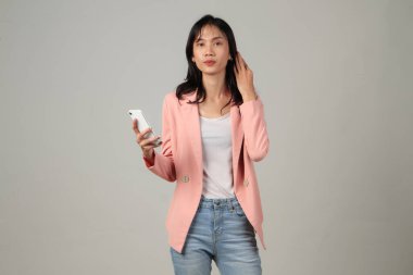 Düşünceli Asyalı kadın resmi kıyafet giyiyor. Elinde cep telefonu var. İzole edilmiş arka planda düşünme hareketi yapıyor.