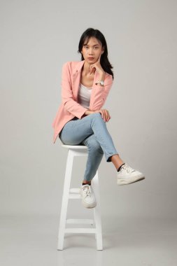 Düşünceli Asyalı kadının taburede oturduğu uzun bir çekim. izole arkaplan