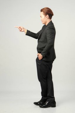 Uzun, mutlu Asyalı iş adamının takım elbise giyip parmak hareketiyle izole edilmiş arka planda yaptığı çekimler.