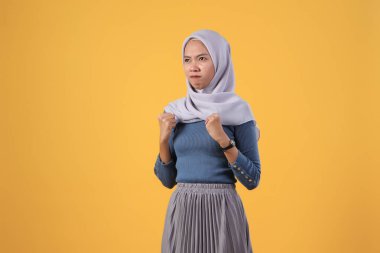 Asyalı kızgın müslüman kadın izole edilmiş sarı arka planda başörtüsü giyiyor.