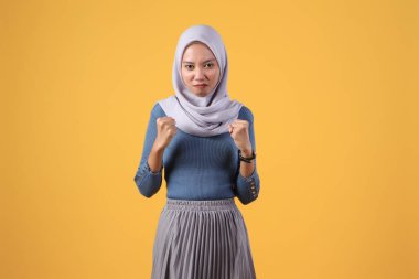 Asyalı kızgın müslüman kadın izole edilmiş sarı arka planda başörtüsü giyiyor.