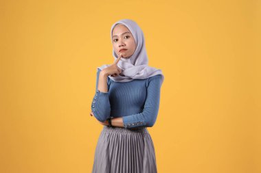İzole edilmiş sarı arka planda düşünceli Asyalı Müslüman kadın.