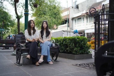 Sokağın kenarında oturan iki Asyalı kadın.