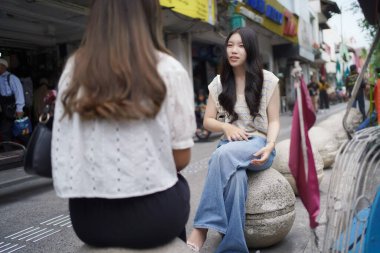 Sokağın kenarında oturan iki Asyalı kadın.