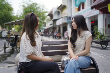 Sokağın kenarında oturan iki Asyalı kadın.
