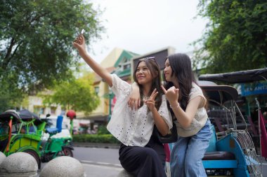 İki mutlu Asyalı kadın Malioboro Caddesi, Yogyakarta, Endonezya 'da akıllı telefonla selfie çekiyorlar.