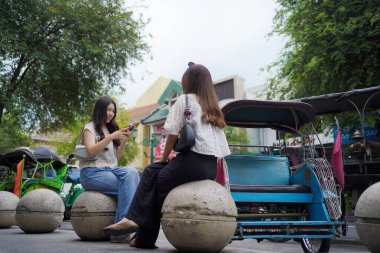Endonezya, Yogyakarta 'da Malioboro caddesinin kenarındaki bankta otururken akıllı telefon tutan iki Asyalı kadın.
