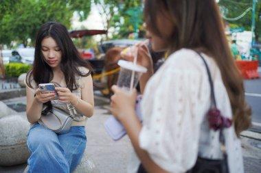 Endonezya, Yogyakarta 'da Malioboro caddesinin kenarındaki bankta otururken akıllı telefon tutan iki Asyalı kadın.