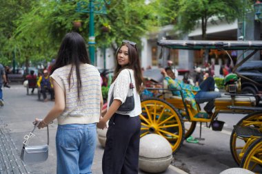 İki Asyalı kadının arka görüntüsü ve Malioboro Caddesi, Yogyakarta, Endonezya 'da yürürken kameraya bakın.