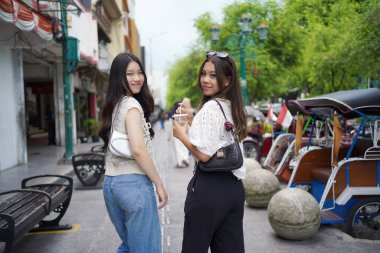 İki Asyalı kadının arka görüntüsü ve Malioboro Caddesi, Yogyakarta, Endonezya 'da yürürken kameraya bakın.