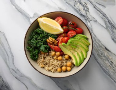 Kinoa, avokado dilimleri, kiraz domatesleri, lahana, kavrulmuş nohut ve limon dilimleri ile dolu renkli ve canlı sağlıklı bir yemek kasesinin yukarıdan görünüşü.