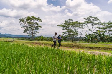 Kırsal bölgede koşarken ellerinde su şişesi tutan aktif Asyalı genç çift.