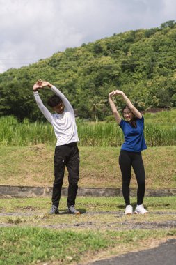 Aktif genç Asyalı çift kırsal alanda egzersiz yapmadan önce geriniyor.