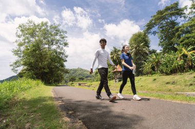 Kırsal bölgede yürürken su şişesi tutan aktif genç Asyalı çift.