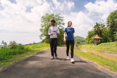 Kırsal bölgede yürürken su şişesi tutan aktif genç Asyalı çift.