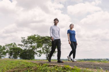 Kırsal bölgede yürürken su şişesi tutan aktif genç Asyalı çift.