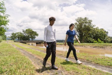 Kırsal bölgede yürürken su şişesi tutan aktif genç Asyalı çift.