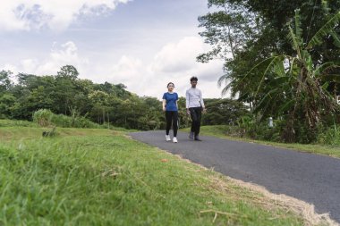 Kırsal bölgede yürürken su şişesi tutan aktif genç Asyalı çift.