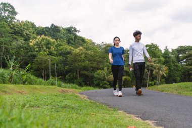 Kırsal bölgede yürürken su şişesi tutan aktif genç Asyalı çift.