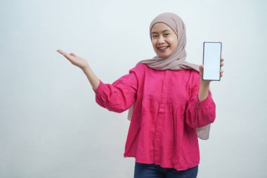 Hijab 'da kendine güvenen genç Asyalı kadın Beyaz Arkaplanda izole edilmiş boş ekranlı akıllı telefonu sunuyor.
