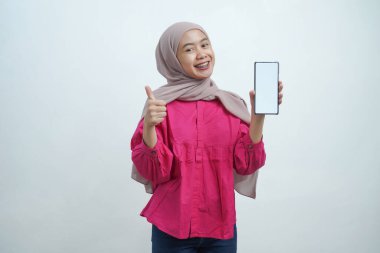 Beyaz arkaplanda izole edilmiş Boş Ekran ve Başparmağıyla Akıllı Telefon Gösteren Mutlu Asyalı Müslüman Kadın