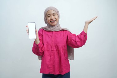Hijab 'da kendine güvenen genç Asyalı kadın Beyaz Arkaplanda izole edilmiş boş ekranlı akıllı telefonu sunuyor.