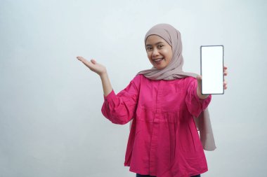 Hijab 'da kendine güvenen genç Asyalı kadın Beyaz Arkaplanda izole edilmiş boş ekranlı akıllı telefonu sunuyor.