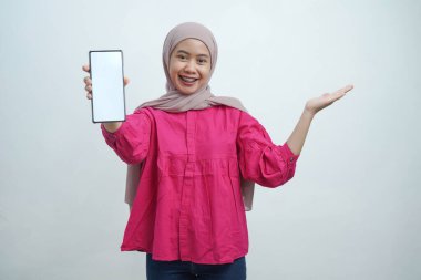 Hijab 'da kendine güvenen genç Asyalı kadın Beyaz Arkaplanda izole edilmiş boş ekranlı akıllı telefonu sunuyor.