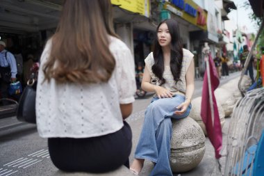 Sokağın kenarında oturan iki Asyalı kadın.