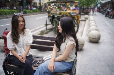 Sokağın kenarında oturan iki Asyalı kadın.