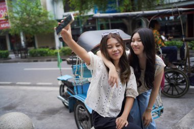 İki mutlu Asyalı kadın Malioboro Caddesi, Yogyakarta, Endonezya 'da akıllı telefonla selfie çekiyorlar.