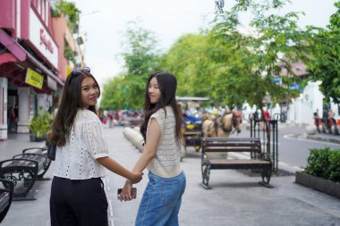 İki Asyalı kadının arka görüntüsü ve Malioboro Caddesi, Yogyakarta, Endonezya 'da yürürken kameraya bakın.