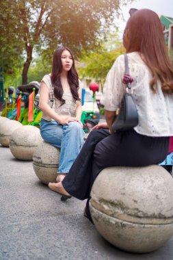 Genç Asyalı bir kadın, canlı bir şehir sokağında arkadaşıyla konuşurken gülüyor. Gerçek bağlantının ve arkadaşlığın neşeli anı.