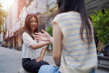 Genç Asyalı bir kadın, canlı bir şehir sokağında arkadaşıyla konuşurken gülüyor. Gerçek bağlantının ve arkadaşlığın neşeli anı.