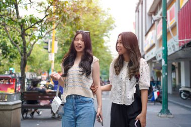 İki neşeli Asyalı kadın şehrin kaldırımında el ele yürüyorlar. Sohbet ederken ve gülümserken, şehir ortamında güneşli bir günün tadını çıkarırken buzlu bir içki içilir..