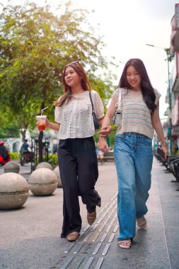 İki neşeli Asyalı kadın şehrin kaldırımında el ele yürüyorlar. Sohbet ederken ve gülümserken, şehir ortamında güneşli bir günün tadını çıkarırken buzlu bir içki içilir..