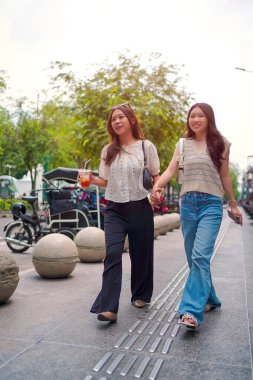 İki neşeli Asyalı kadın şehrin kaldırımında el ele yürüyorlar. Sohbet ederken ve gülümserken, şehir ortamında güneşli bir günün tadını çıkarırken buzlu bir içki içilir..