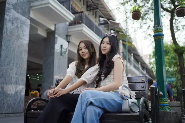 Sokağın kenarında oturan iki Asyalı kadın.