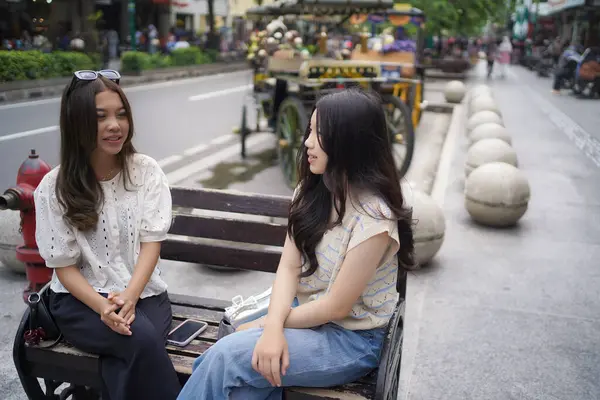 Sokağın kenarında oturan iki Asyalı kadın.