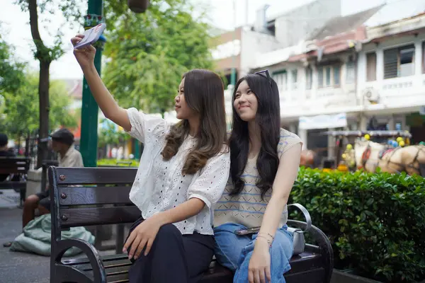 İki mutlu Asyalı kadın Malioboro Caddesi, Yogyakarta, Endonezya 'da akıllı telefonla selfie çekiyorlar.