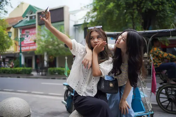 İki mutlu Asyalı kadın Malioboro Caddesi, Yogyakarta, Endonezya 'da akıllı telefonla selfie çekiyorlar.