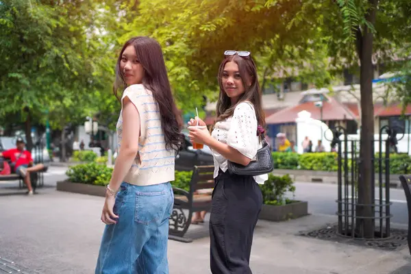 İki zarif Asyalı kadın kameraya gülümserken canlı bir şehir caddesinde çekçekçeklerle yürüyorlar..